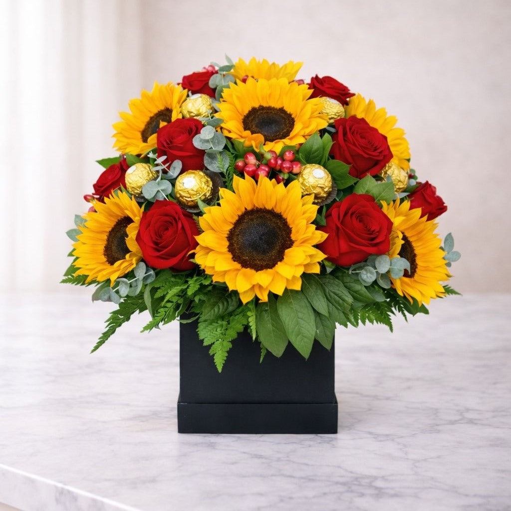 Arreglo floral con girasoles amarillos, rosas rojas y follaje verde en caja negra elegante, disponible con flores a domicilio en Monterrey para cumpleaños y ocasiones especiales.