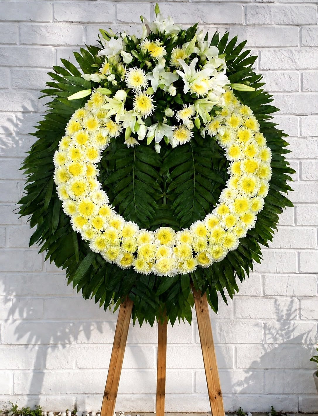 Corona fúnebre con lirios blancos, flores blancas y follaje verde para condolencias, con entrega a domicilio en Monterrey | Pink Rose Florería
