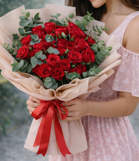 Mujer sosteniendo un elegante ramo de rosas rojas con follaje y envoltura beige disponible con envío de flores a domicilio en Monterrey.